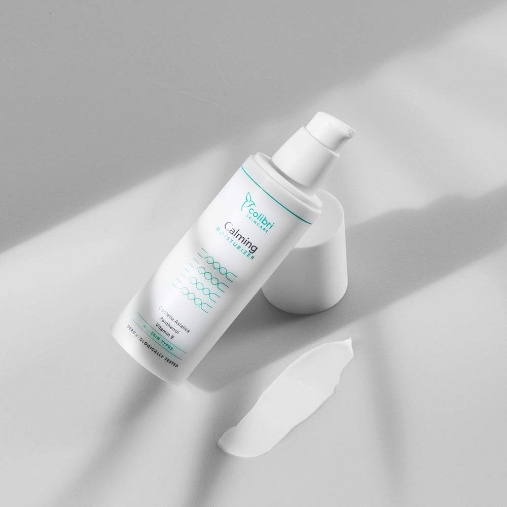 Flasche mit Feuchtigkeitscreme und Klecks auf einer grauen Oberfläche im sanften Licht.