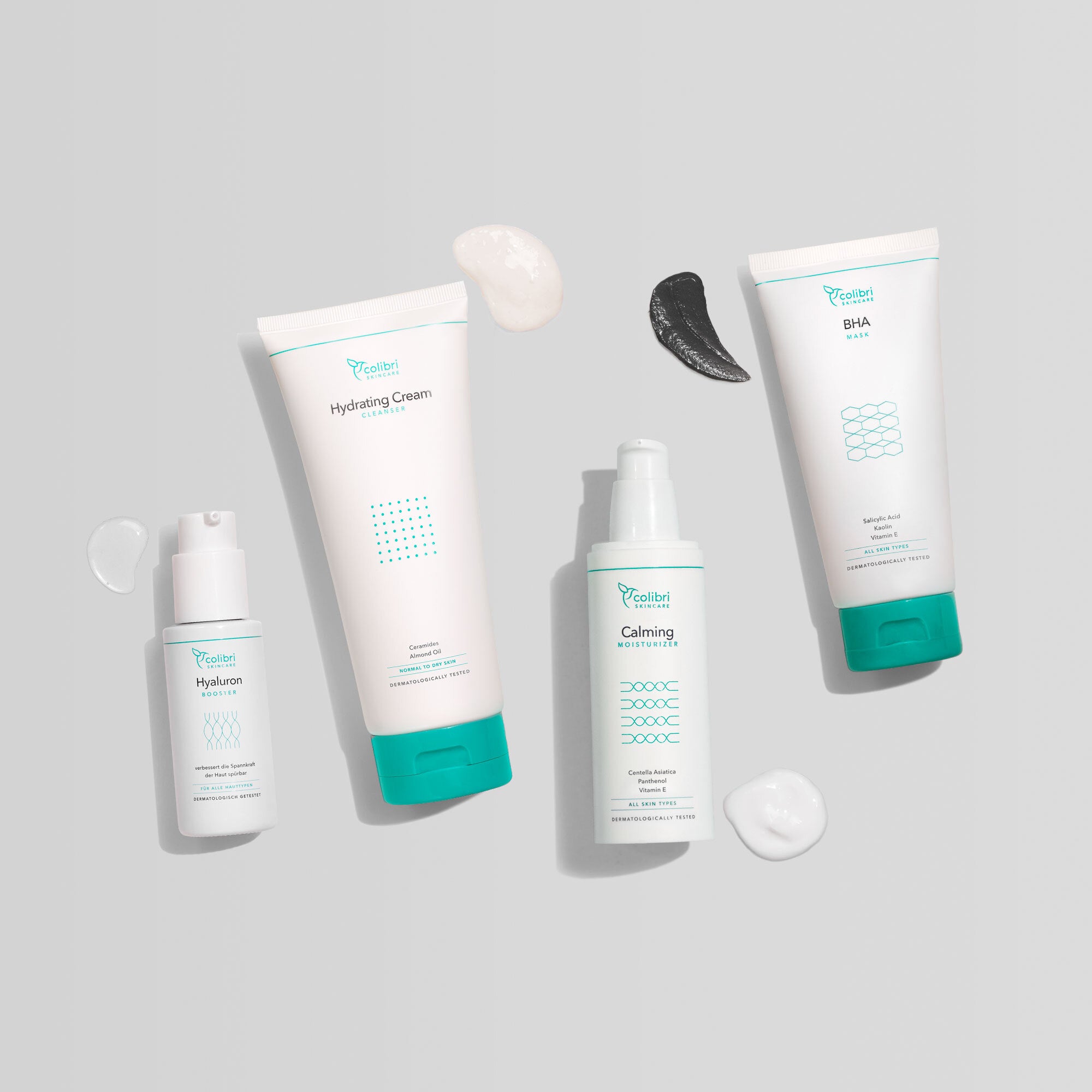 Vier Kosmetikprodukte in weißen Flaschen und Tuben mit türkisfarbenen Details auf grauem Hintergrund.