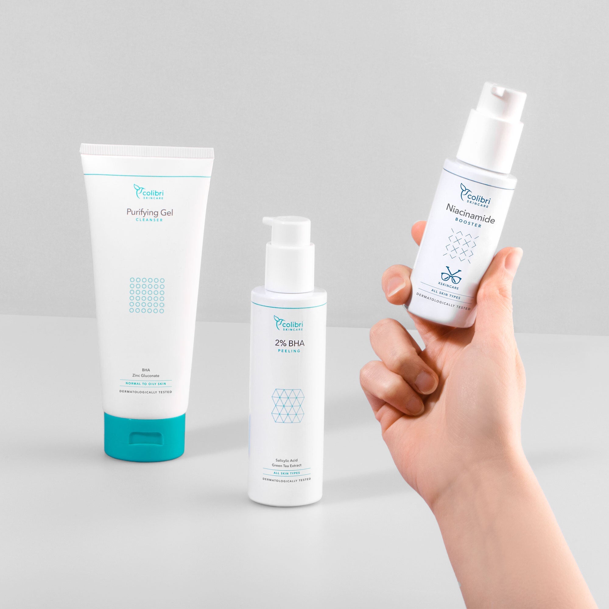 Hand hält eine Flasche Niacinamid neben zwei anderen Hautpflegeprodukten auf einem Tisch.