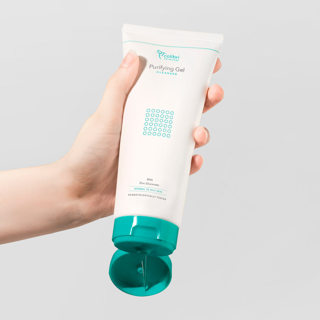 Hand hält eine Tube eines Reinigungsgels mit türkisfarbenem Deckel, aus der etwas Gel herausgedrückt wird.