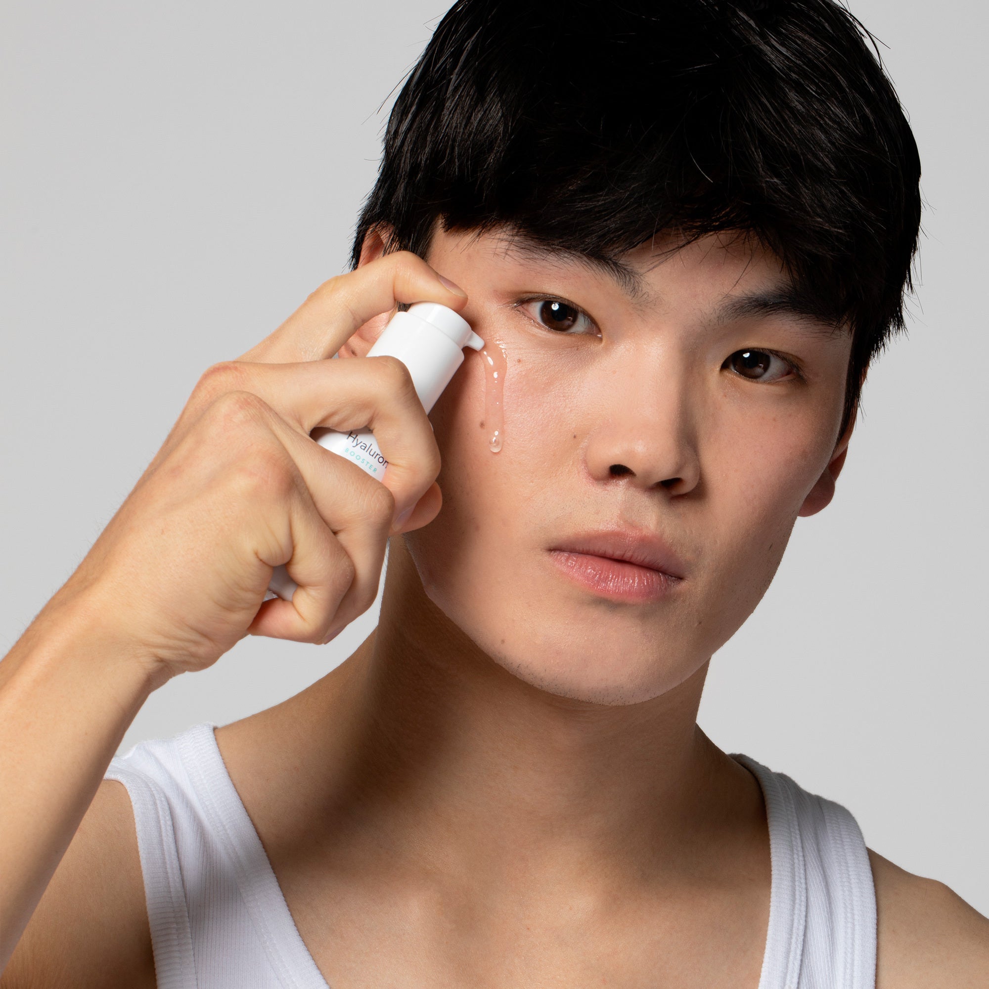 Ein junger Mann trägt eine Flüssigkeit aus einer Flasche auf sein Gesicht auf und schaut in die Kamera.