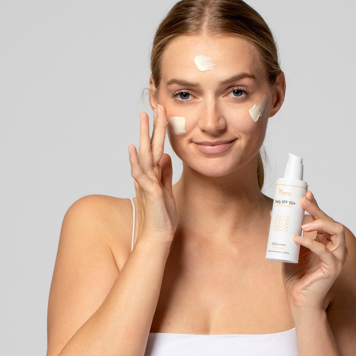 Frau trägt Sonnencreme auf ihr Gesicht auf und hält eine Flasche mit der Aufschrift "Daily SPF 50+."