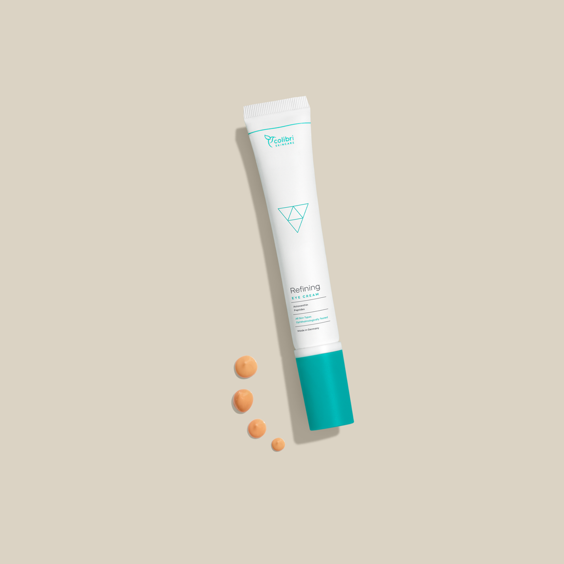 Eine Tube Augencreme mit türkisfarbener Kappe und vier Tupfen der Creme auf einem beigen Hintergrund.